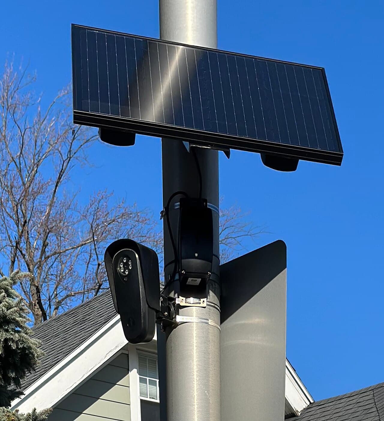 A Flock Safety license plate reader: black camera on a slim pole with a tilted solar panel on top